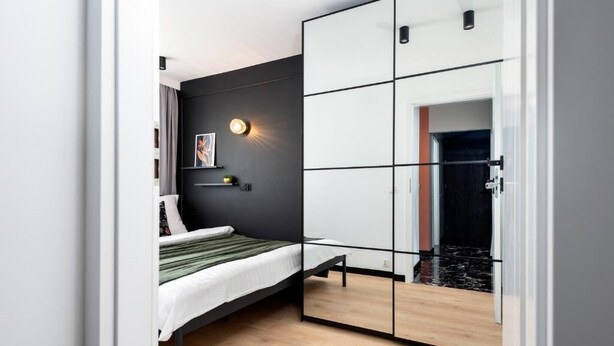 Een moderne slaapkamer met een bed, een garderobe met spiegeldeuren, een wandlamp en een schilderij.
