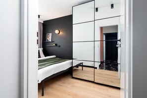 Une chambre à coucher moderne avec un lit, une armoire aux portes miroir, un luminaire fixé au mur et un tableau.