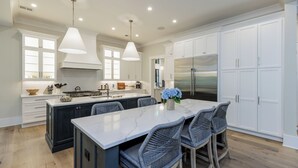 Een moderne keuken met witte kastjes, een groot eiland met barstoelen en een roestvrijstalen koelkast.