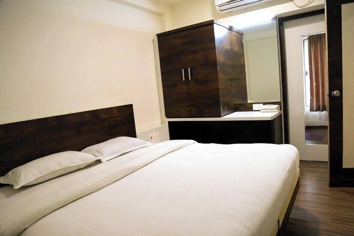 Una habitación de hotel con una cama grande, un armario, un escritorio con espejo y un equipo de aire acondicionado.