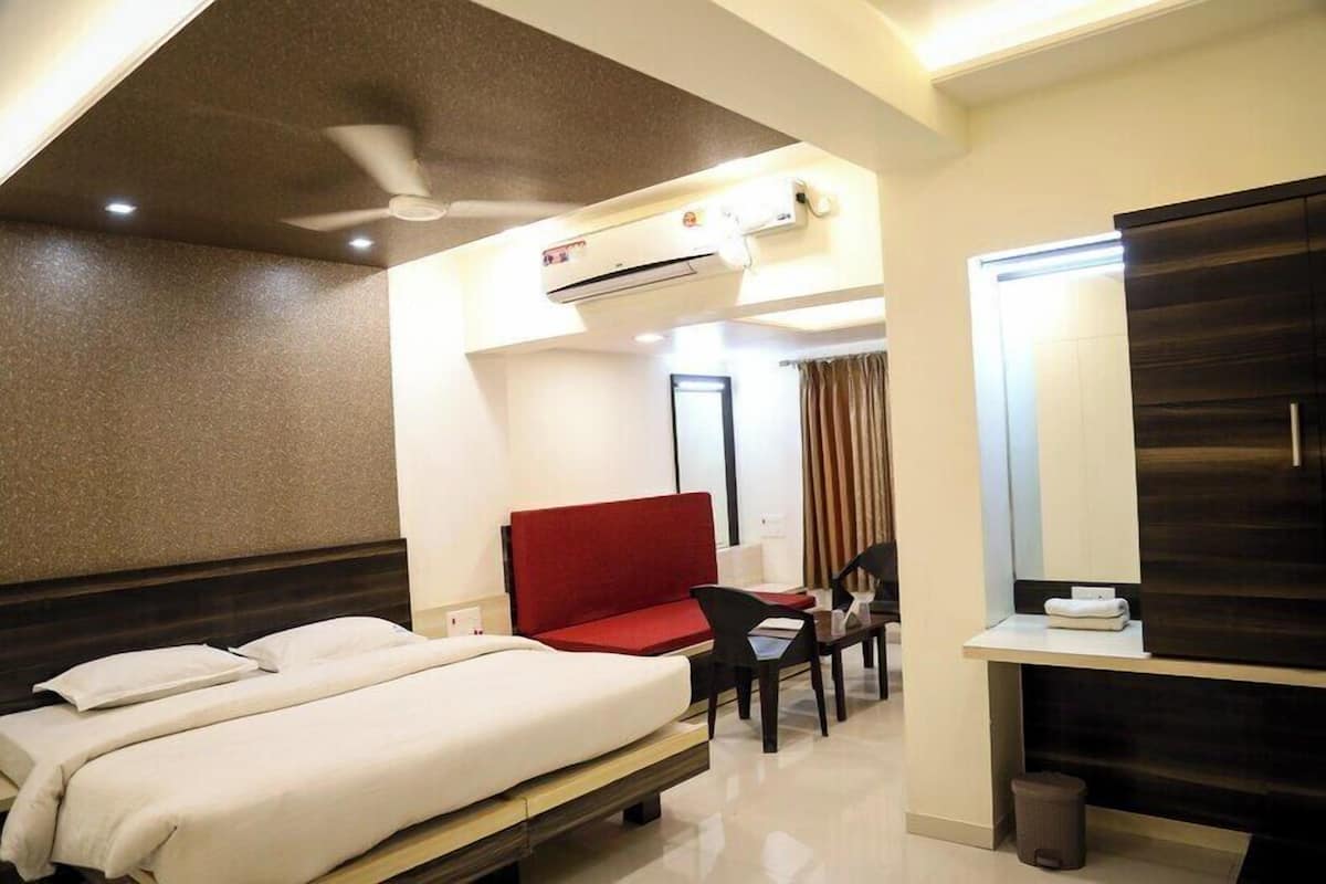 Habitación de hotel con cama, sofá rojo, escritorio con silla, espejo y unidad de aire acondicionado.