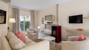 A modern living room with a sofa, armchairs, a TV, a fireplace, and a large window with curtains.