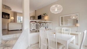 A modern hotel room with a dining area featuring white furniture, a staircase, and a large window with curtains.