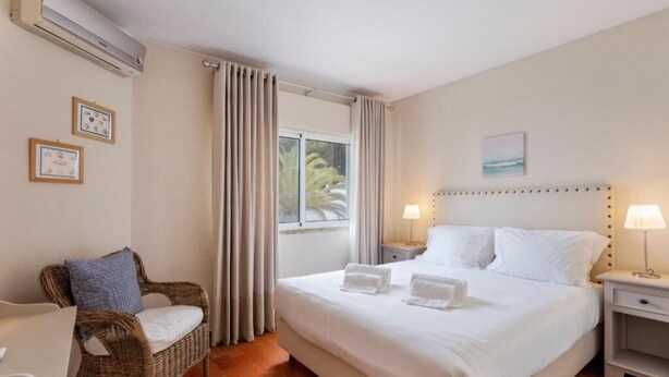 A hotel room with a large bed, a wicker chair, a small table, and a window with curtains.