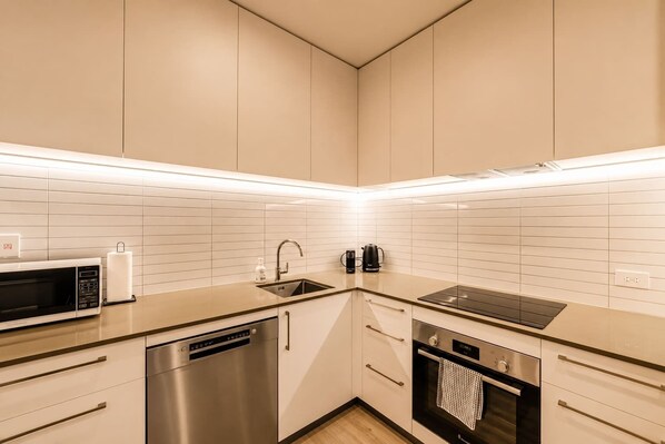 A modern kitchen with white cabinetry, a stainless steel dishwasher, a built-in oven, and a microwave.