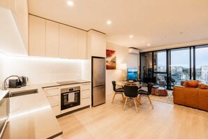 A modern kitchen with a dining area, a sofa, and a large window offering a city view.
