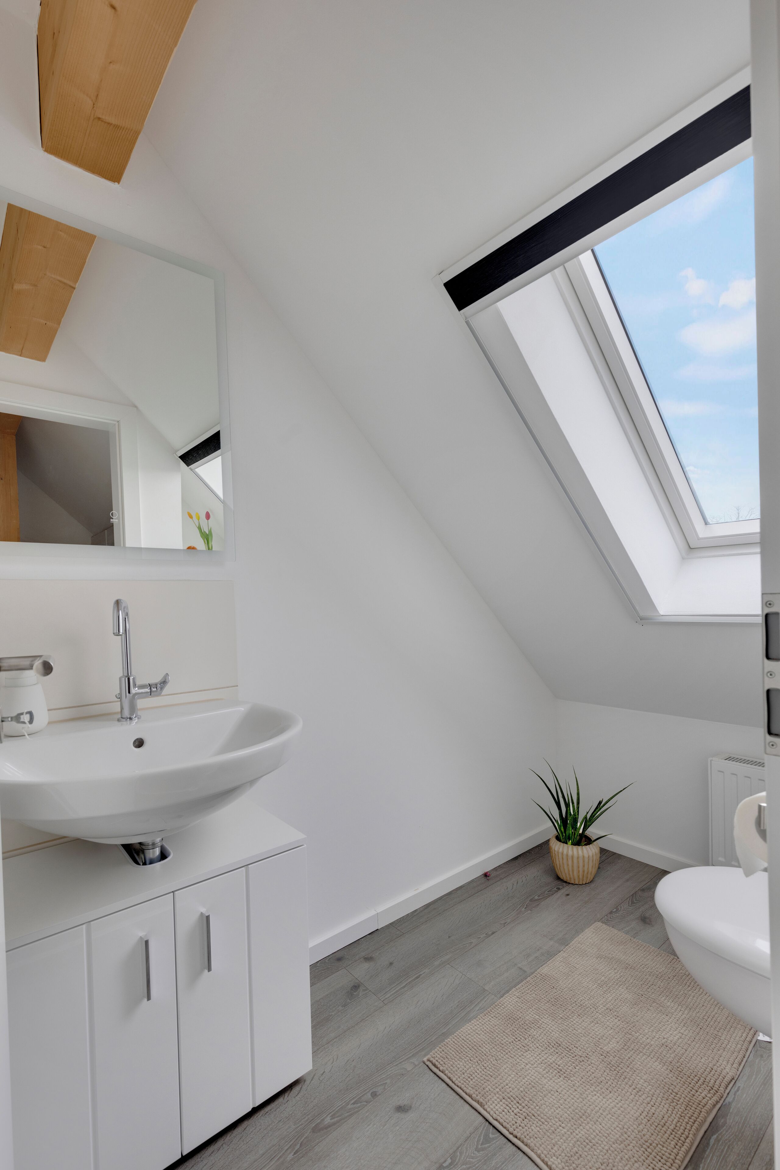 Un baño moderno con tragaluz, muebles blancos y un espejo grande.