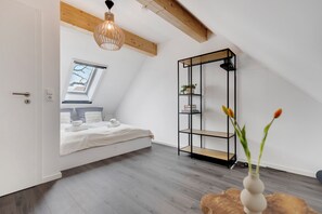 A bedroom with a skylight, a bed, a wooden floor, a black metal shelving unit, and a vase with flowers. - Vacation home SeeZeit with garden, up to 6 people, 500 meters to the lake (Hüde, Niedersachsen, Deutschland)