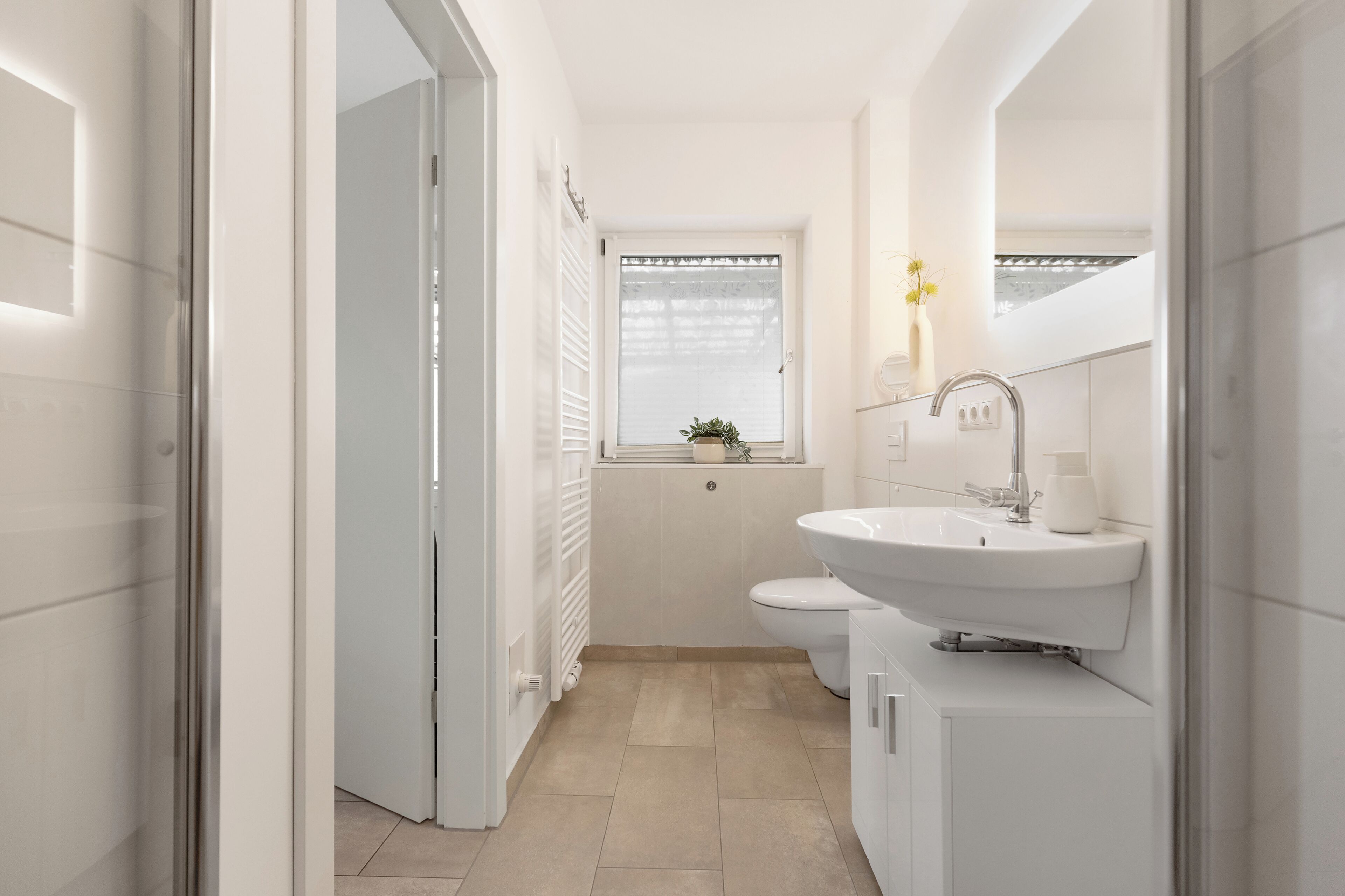 Ein modernes Badezimmer mit einem weißen Waschbecken, einer Toilette und einem Fenster mit Pflanze.