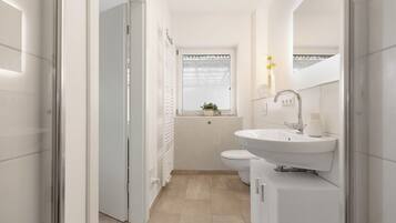 Ein modernes Badezimmer mit einem weißen Waschbecken, einer Toilette und einem Fenster mit Pflanze.