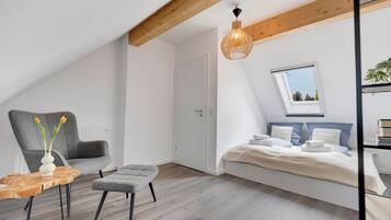 Una camera da letto moderna con soffitto spiovente, un letto con biancheria da letto bianca, una poltrona grigia, un piccolo tavolino e una lampada a sospensione.
