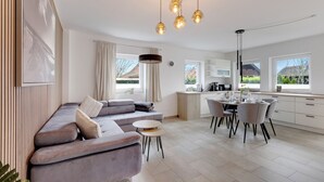 A modern kitchen with a dining area, a sofa, and a view of the outdoors.