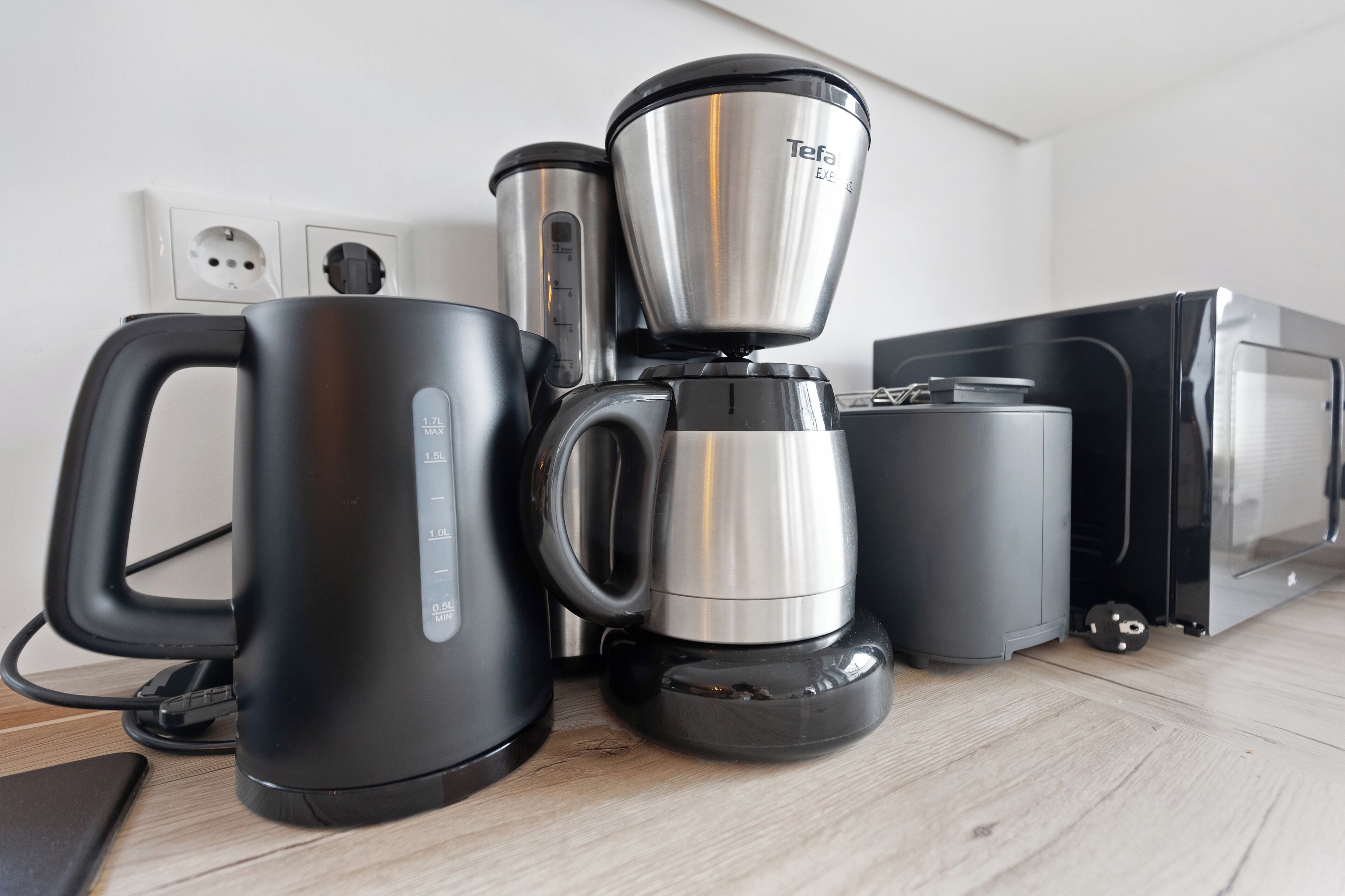 A kitchen with a coffee maker, a kettle, and a microwave.