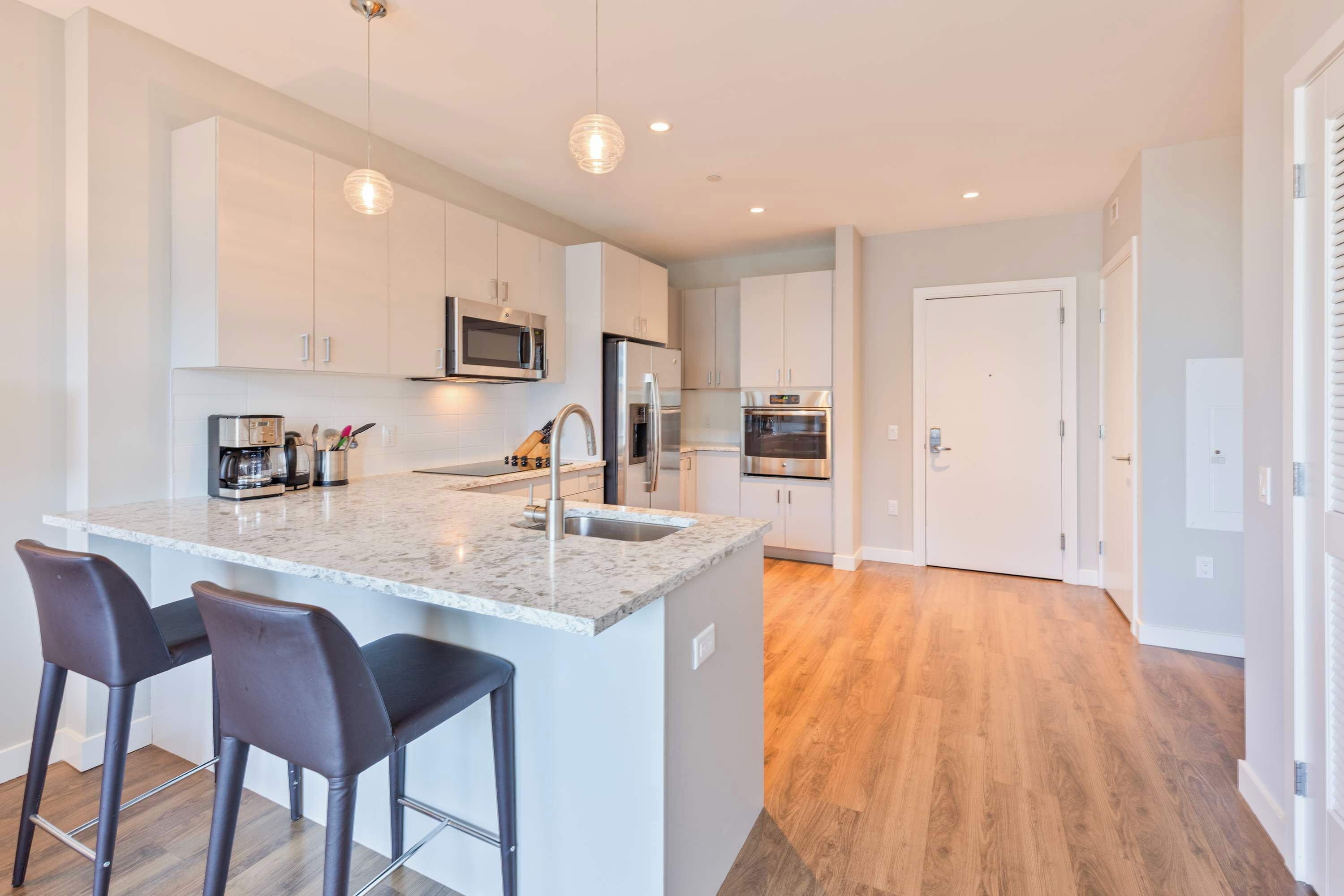 A modern kitchen with white cabinets, stainless steel appliances, and a marble countertop.