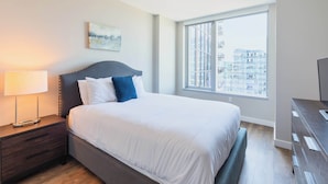 Una habitación de hotel moderna con una cama grande, una mesita de noche, un aparador y una ventana con vistas a la ciudad.