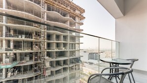 Un edificio de gran altura en construcción, con varios pisos a la vista, un balcón con barandilla de vidrio y una mesa con sillas.