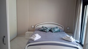 A neatly made bed with pillows, a bedside table, and a window with curtains. - Apartment 204 (Messina)