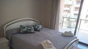 A neatly made bed with a patterned bedspread, two pillows, and folded towels on a white headboard. - Apartment 204 (Messina)