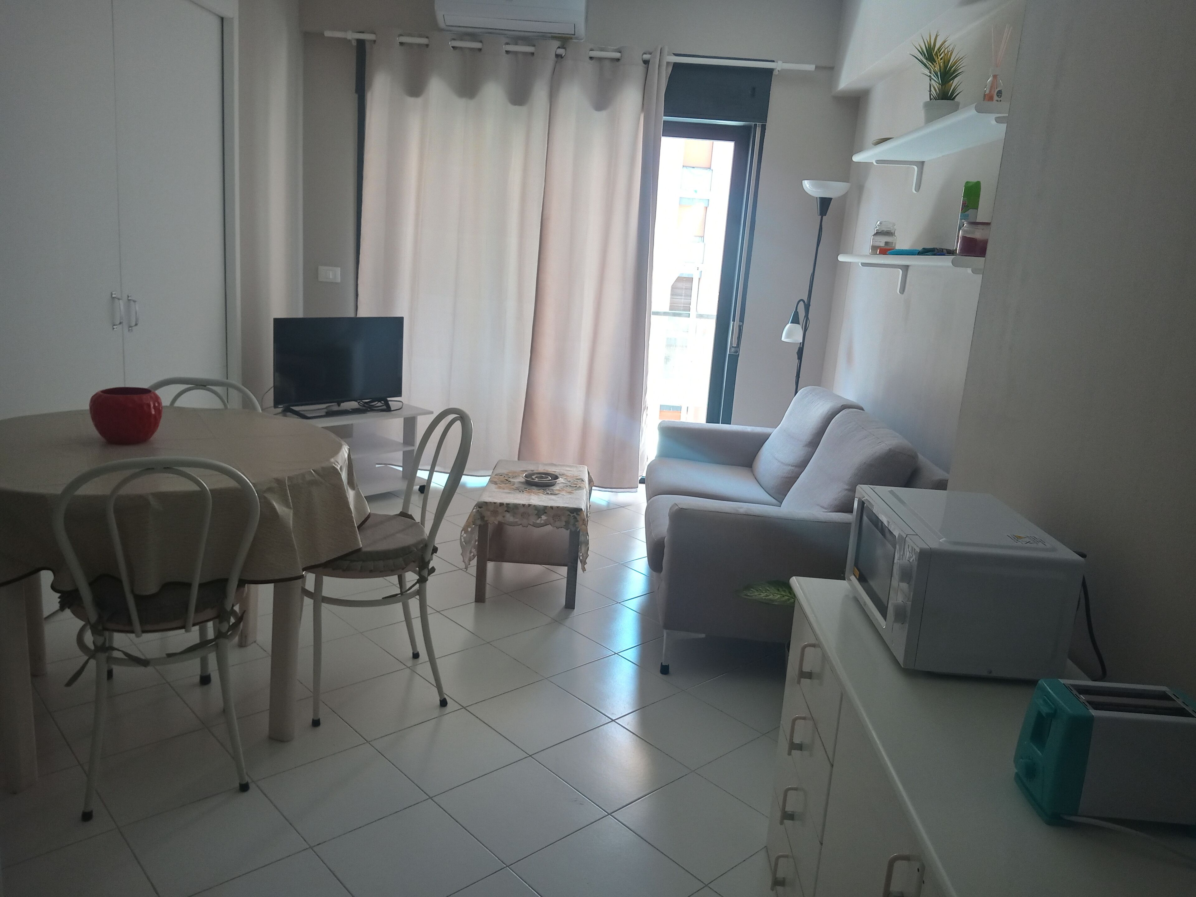 Una sala de estar con una mesa de comedor, sillas, un sofá, un televisor y una zona de cocina con un tostador.