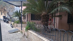 A paved sidewalk with a metal fence, a palm tree, and parked scooters. - Apartment 204 (Messina)