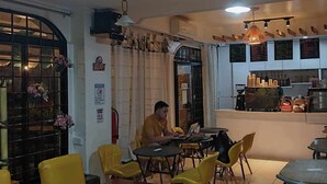L’intérieur d’un restaurant avec des chaises jaunes, un homme travaillant sur un ordinateur portable et un comptoir où est affiché le menu.