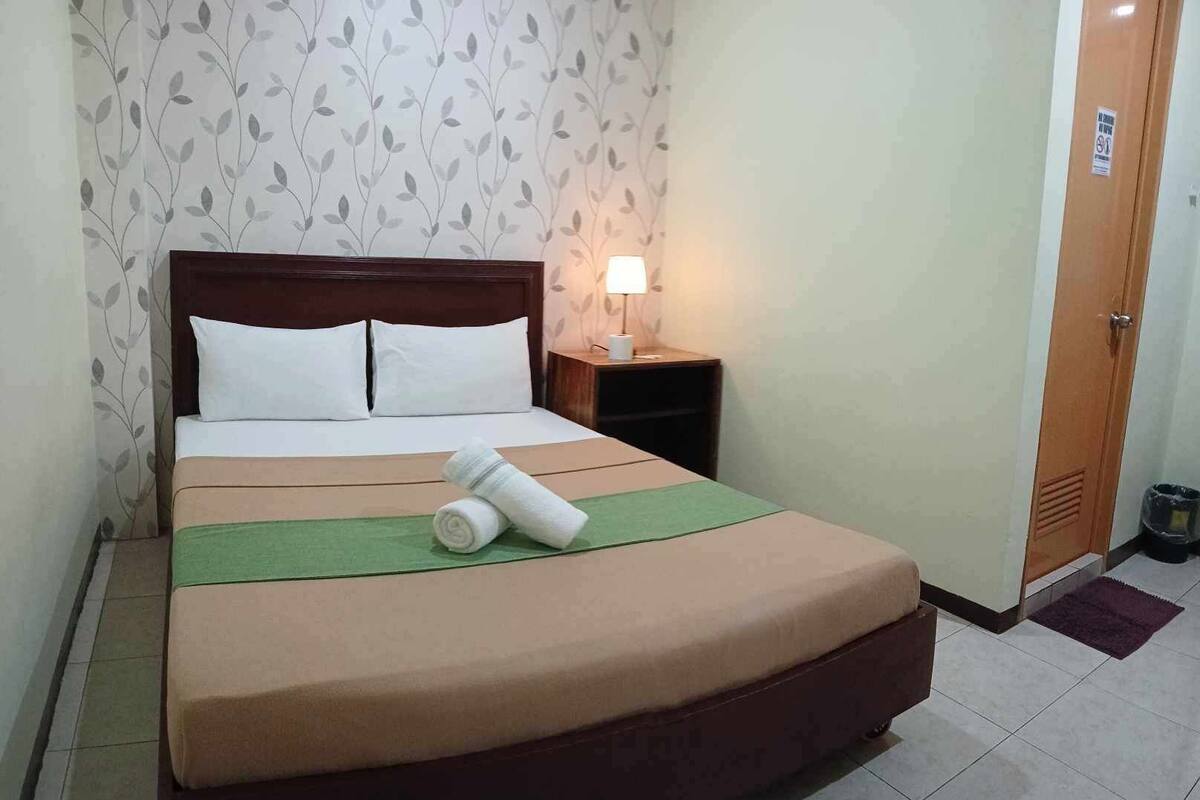 A hotel room with a bed, a nightstand, a lamp, and a door.