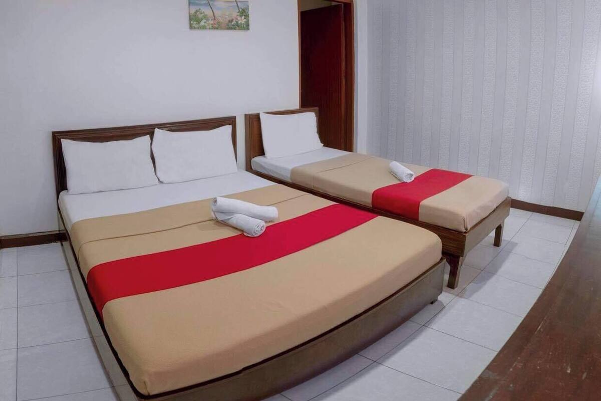A hotel room with a large bed, a smaller bed, and a bench.