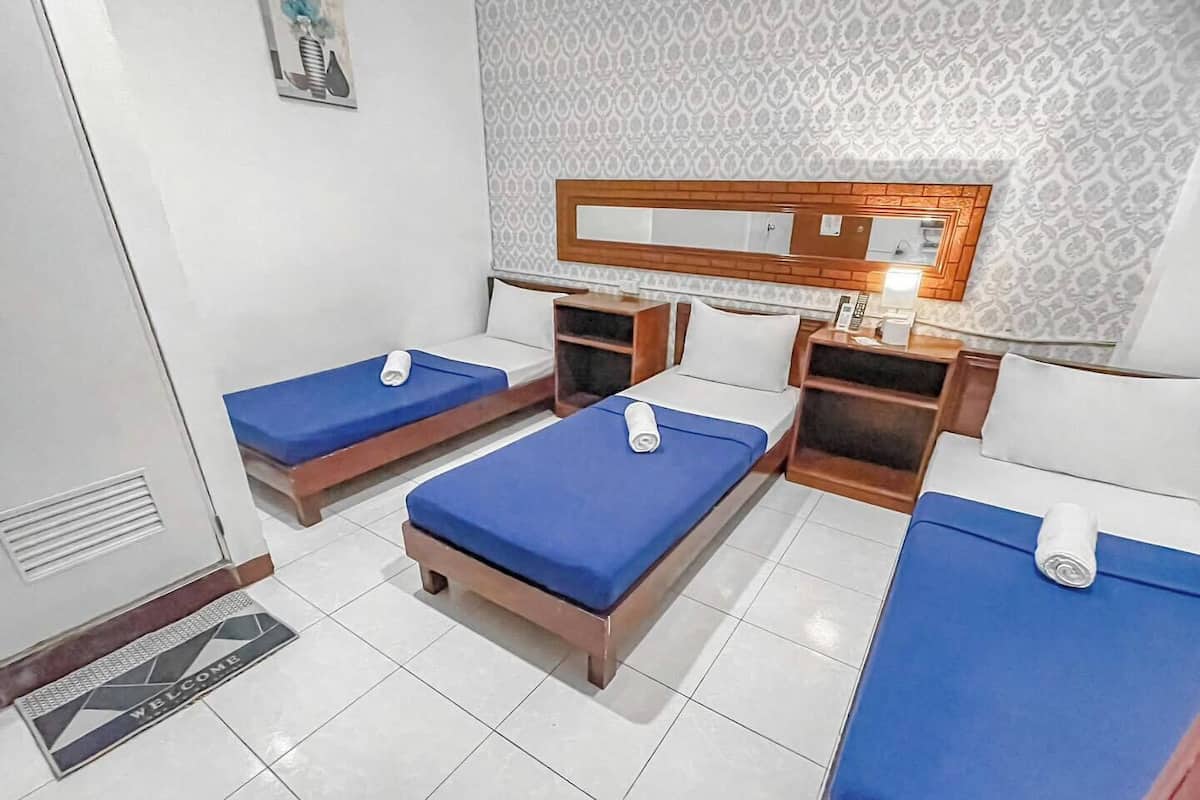 A hotel room with two single beds, a small desk, a mirror, and a patterned wallpaper.