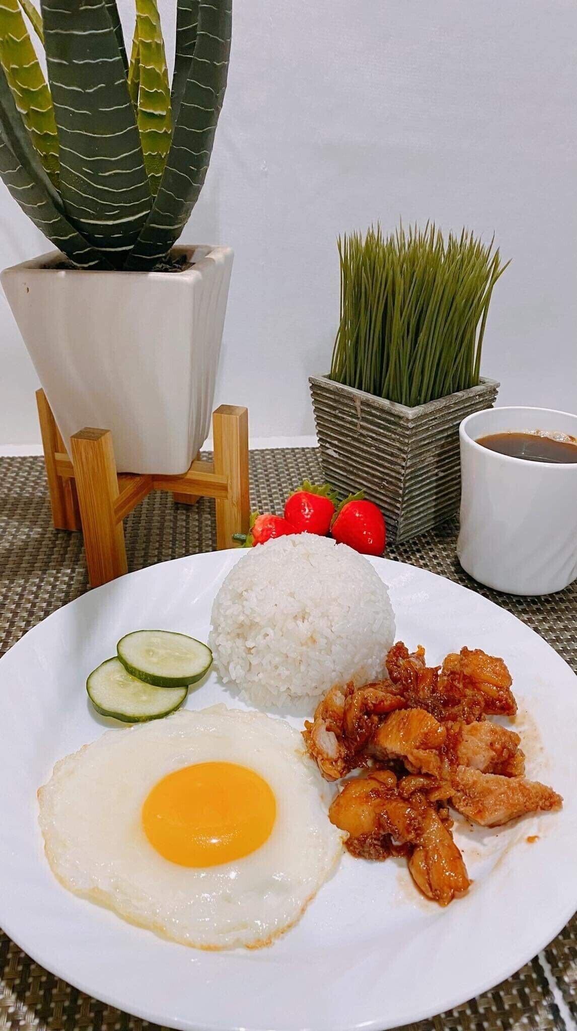 Un plato de comida con arroz, huevo frito, rodajas de pepino y pollo.
