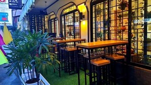 Un espace intérieur accueillant, aménagé avec des tables et des chaises en bois, et entouré de grandes fenêtres ornées de panneaux de verre décoratifs.
