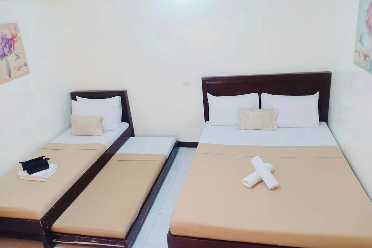 A hotel room with two single beds, each with a wooden headboard, beige bedding, and a small table with a black item on it.