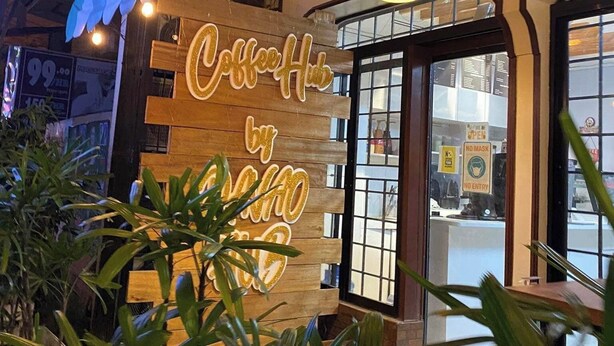 Un café avec une enseigne au néon indiquant « Coffee Hub by Techo » et une façade en bois.