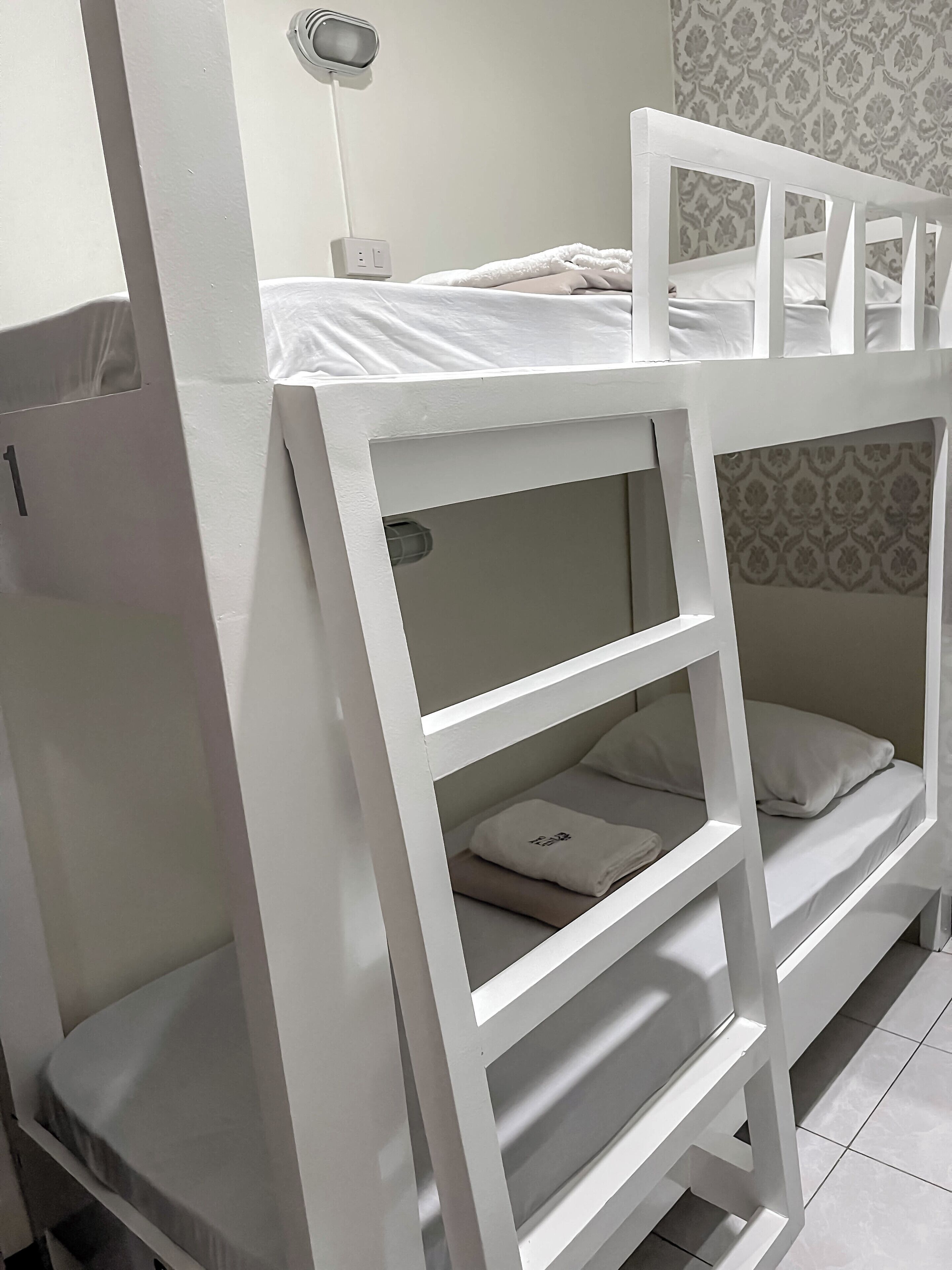 A bunk bed with a ladder, a bedside table, and a wall-mounted lamp.