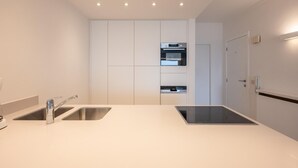 A modern kitchen with two sinks, a built-in oven, and a door leading to another room. - Spacious Seaside Apartment (Knokke-Heist)