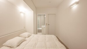 A minimalist bedroom with a large bed, a door, and a mirror. - Spacious Seaside Apartment (Knokke-Heist)