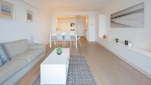 A modern living room with a sofa, a coffee table, and a dining area with chairs and a table. - Spacious Seaside Apartment (Knokke-Heist)