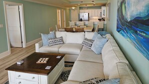 A living room with a sectional sofa, a coffee table, and a painting on the wall. - Holiday Isle SandDollar 713 (Dauphin Island)
