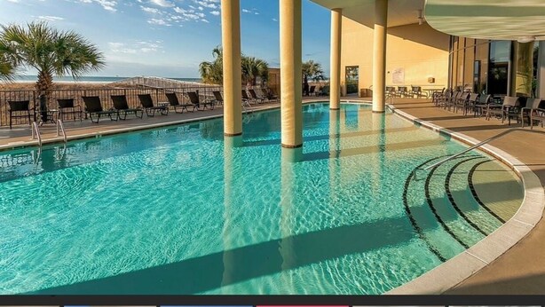 A pool area with clear water, lounge chairs, and palm trees. - Holiday Isle SandDollar 713 (Dauphin Island)