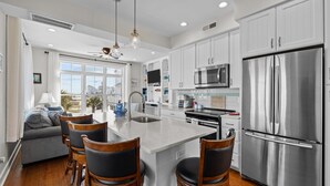 A modern kitchen with white cabinets, stainless steel appliances, and a large island with bar stools. - Exhibit E- Pet Friendly Townhome in Atlantic Beach (Atlantic Beach)