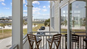 A balcony with two wooden chairs, overlooking a parking lot and a building with large windows. - Exhibit E- Pet Friendly Townhome in Atlantic Beach (Atlantic Beach)