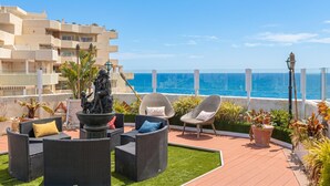 Una terraza en la azotea con mobiliario exterior, una estatua y vistas al océano.