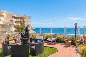 Eine Dachterrasse mit Gartenmöbeln, einer Statue und Blick aufs Meer.