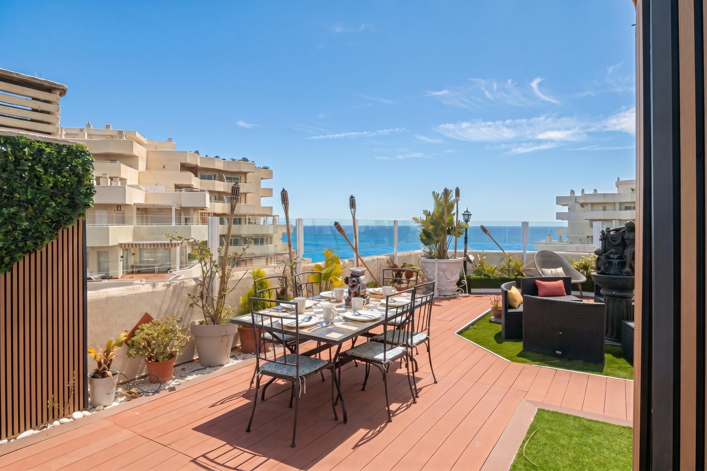 Una terraza con mesa lista para comer, plantas en macetas y mobiliario de exterior.