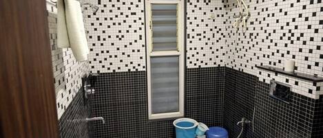 A small bathroom with a toilet, a sink, and a shower. There are two blue buckets and a white toilet paper holder on the wall.