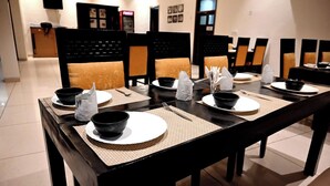 Comedor con una mesa larga dispuesta para varios comensales, con cuencos negros, platos blancos y individuales tejidos.