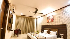 Habitación de hotel con cama, mesita de noche, ventilador de techo y televisión montada en la pared.