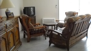 Una sala de estar con un sofá, dos sillones, una mesita, un televisor y una lámpara.