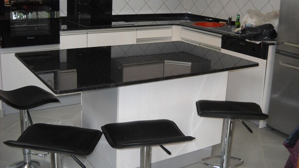 Cocina moderna con encimera negra, armarios blancos y refrigerador de acero inoxidable.