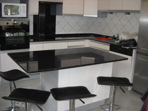 Cocina moderna con encimera negra, armarios blancos y refrigerador de acero inoxidable.