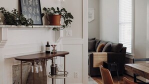 Una sala moderna con chimenea, una mesita de centro y un sofá. Hay plantas en macetas en una estantería e impresión botánica enmarcada en la pared.